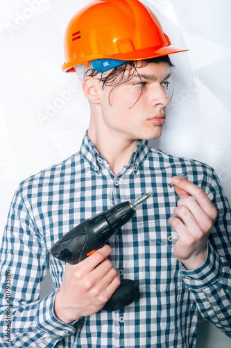 A man in helmet with a screwdriver.Stroitel, designer, designer, architect. Repair in the apartment. Services.Attractive young man in an orange construction helmet