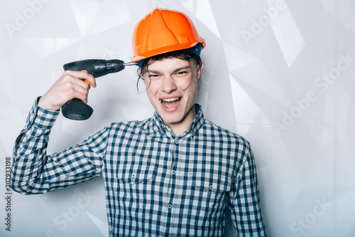 Portrait of young sexy carpenter.Worker, repairs, repairman, strong builder. Man in helmet. Repair and renovation concept. Man with drill.worker with drill screaming rage with the background wall