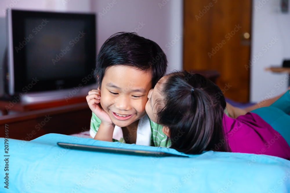 Sister kissing her brother on the cheek while they using tablet. Sister kissing her brother on the cheek while they using tablet.