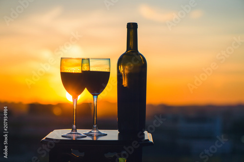 A bottle of wine and two glasses on a sunset background