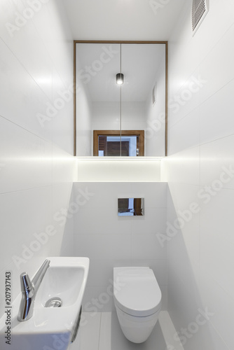 Mirror above toilet in white minimal bathroom interior with washbasin. Real photo