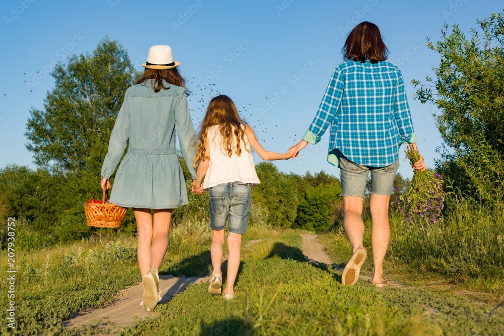 Fototapeta premium Mother and daughter hold hands, walk along the country road.