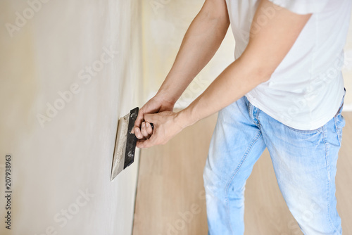 Man plastering the walls with finishing putty in the room.