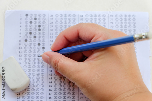 Close up and top view: Answers sheet with blue sharp pencil in hand and rubber isolated on white background. Top view of them. Take the exam timely concept. (selective focus)