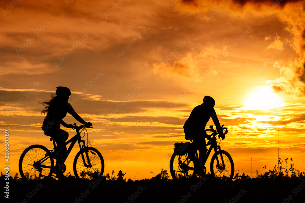 Obraz premium A man and a woman ride bicycles on the road with beautiful colorful sunset sky. Sport and active life concept.