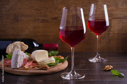 Glasses of wine with cheese, bread, nuts, prosciutto and basil. Wine and food on wooden table. horizontal, room for text