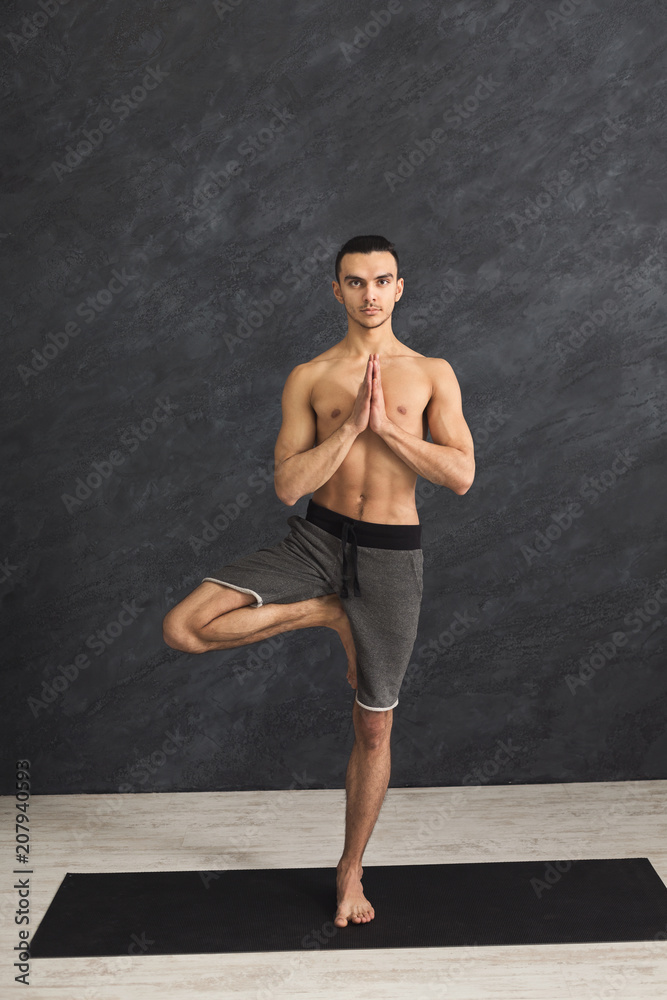Young man training yoga in tree pose Young man training yoga in tree pose