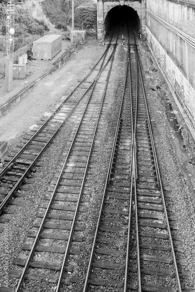 Overhead train tracks merging together going into dark tunnel in black and white.