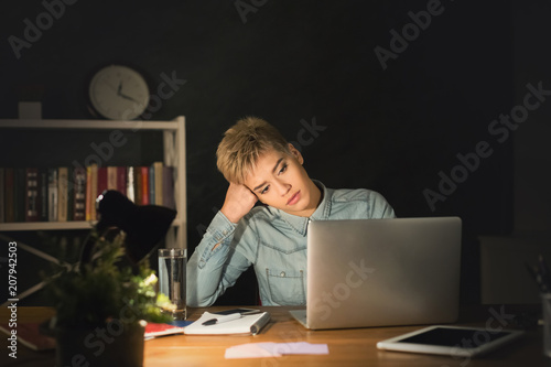 Tired freelancer working on laptop at home until late evening