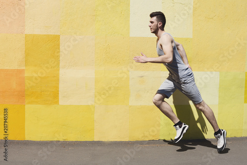 Side view of man running against bright wall
