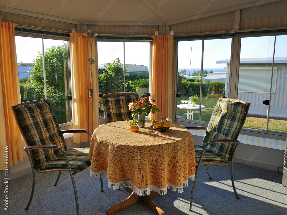 Fototapeta premium Wohnwagen mit einer festen Veranda aus Markisenstoff, Glasschiebefenstern und Jalousien auf einem deutschen Campingplatz. Komfortabel und gepflegt. Innenansicht der Veranda.