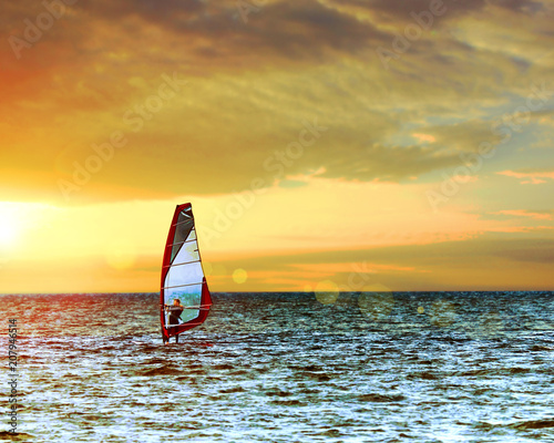 Windsurfer in the sea with a scenic sunset sky. Toned, lens sun flare. Active sport vacation concept