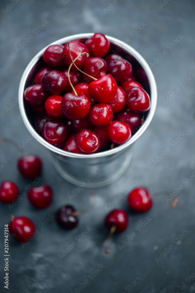 Cherries with a small metal bucket on a grey concrete background, summer berries concept with copy space. Neutral color tones still life Cherries with a small metal bucket on a grey concrete background, summer berries concept with copy space. Neutral color tones still life