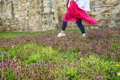 Woman in pink dress walking on meadow full of spring flowers, enjoying nice weather,  fresh air and nature