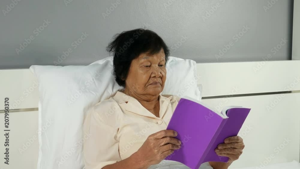 4k of old woman reading a book on bed in bedroom