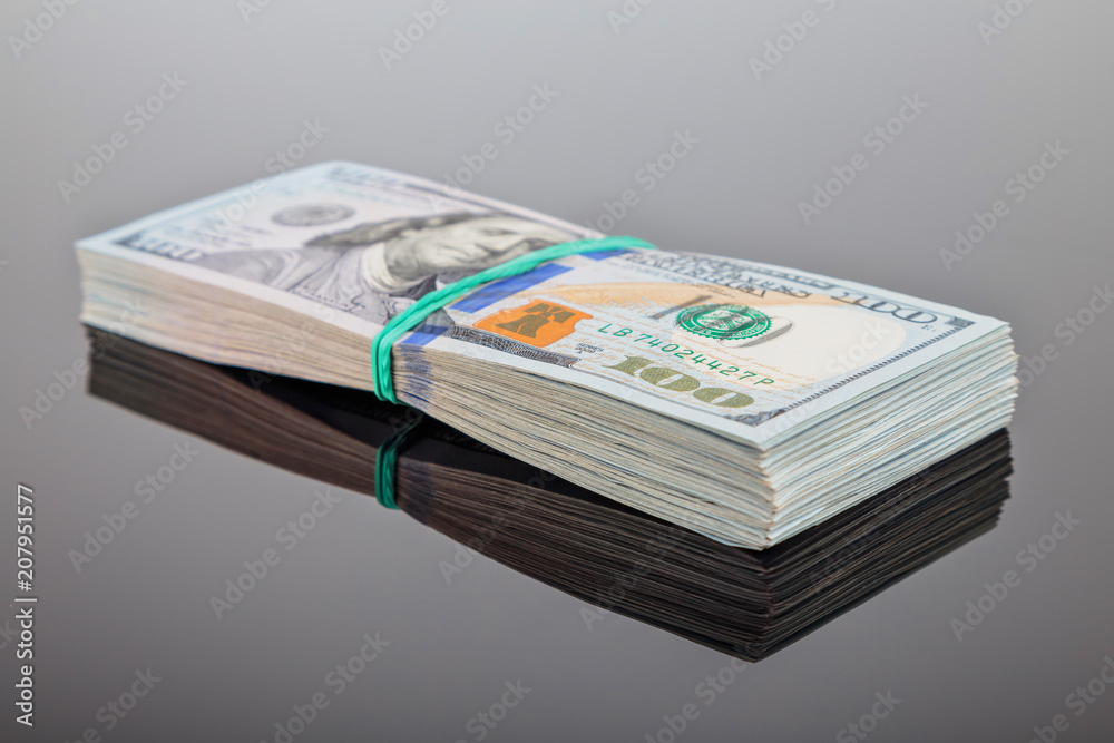 pack of 100 $ banknotes tied with an elastic band lies on a dark mirror surface pack of 100 $ banknotes tied with an elastic band lies on a dark mirror surface