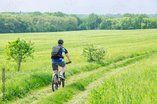 man riding bicycle by trail in green barley field. copy space