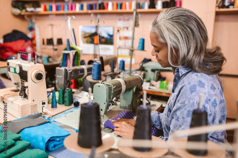 Mature woman sitting in her workshop using a sewing machine Mature woman sitting in her workshop using a sewing machine