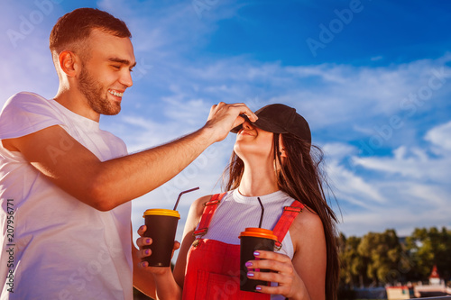 Happy couple having fun in the city at sunset. Laughing young man and woman holding coffee cups