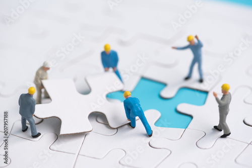 miniature people team trying to complete the last jigsaw puzzle piece , teamwork concept photo