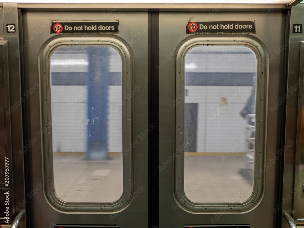 Windows of a moving subway train looking out into station platform upon departure