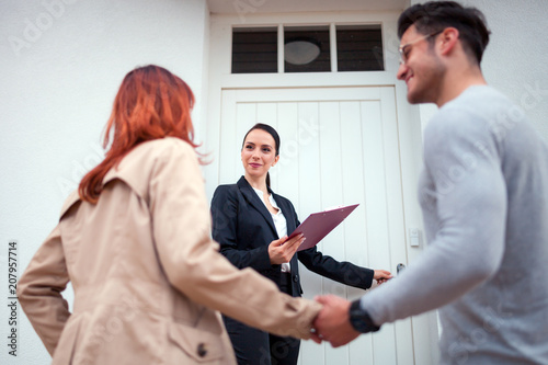 Принти на полотні Real estate agent near door inviting young couple to enter house for visit