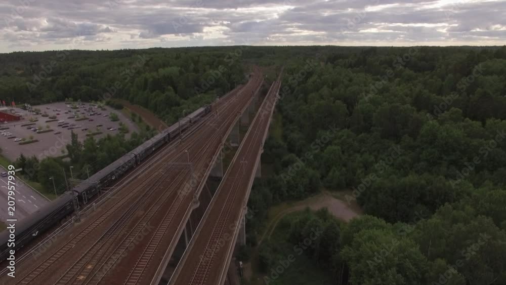 Aerial view of commuter train passing by over railway bridge in Sweden. Drone shot of railroad travel transportation Aerial view of commuter train passing by over railway bridge in Sweden. Drone shot of railroad travel transportation