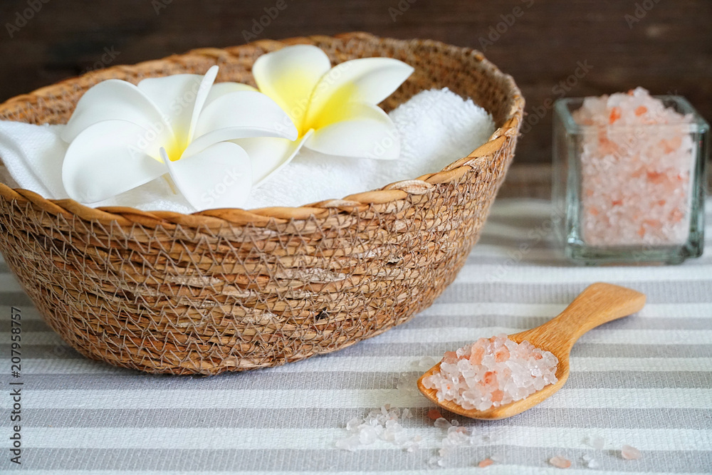 Close up topview himalayan pink salt in the spoon and white towel in the basket decorate with white flower on spa table. Close up topview himalayan pink salt in the spoon and white towel in the basket decorate with white flower on spa table.