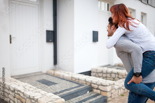Man carrying wife on his back in front of their new home, happy couple after buying real estate © leszekglasner