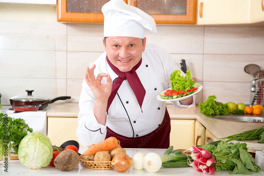 Male chef, shows a sign Ok standing in the kitchen. Prepare a delicious salad of fresh vegetables. Male chef, shows a sign Ok standing in the kitchen. Prepare a delicious salad of fresh vegetables.