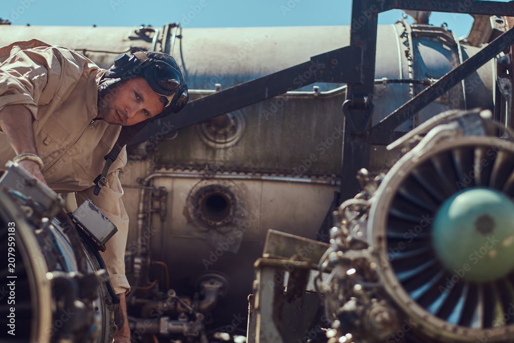 Portrait of a mechanic in uniform and flying helmet, repairing the dismantled airplane turbine in an open-air museum.