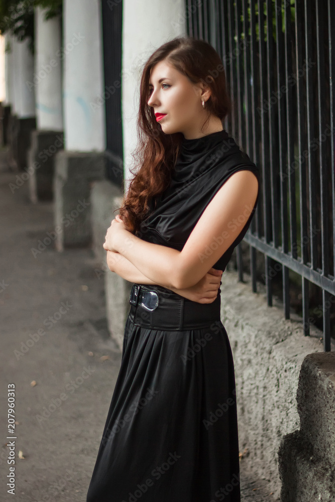 beautiful, young girl in a black dress with a corset on a background of a fence with clones. A model with clean skin. beautiful, young girl in a black dress with a corset on a background of a fence with clones. A model with clean skin.