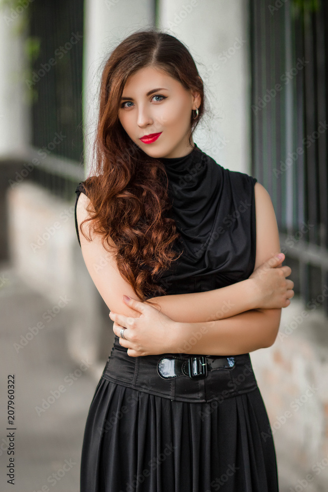 beautiful, young girl in a black dress with a corset on a background of a fence with clones. A model with clean skin.