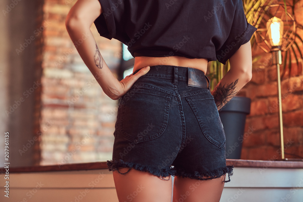 Cropped shot of a slim sexy girl showing her butt in black shorts and  t-shirt, posing in studio with loft interior. Stock Photo | Adobe Stock
