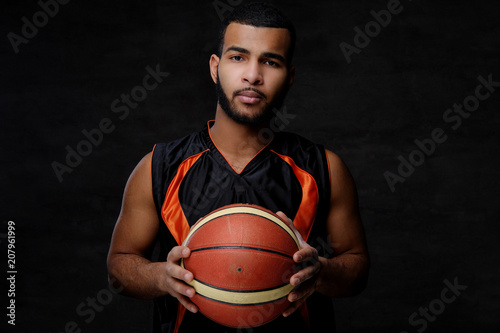 Young African-American basketball player in sportswear isolated over dark background.