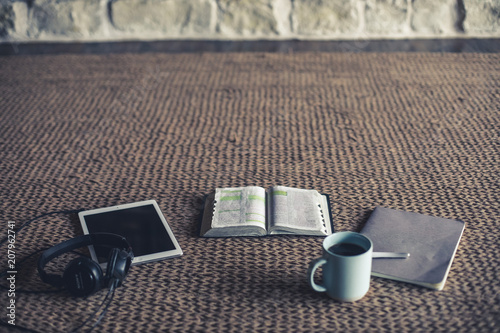 Photo of open Bible, coffee, notepad and tablet on a rug