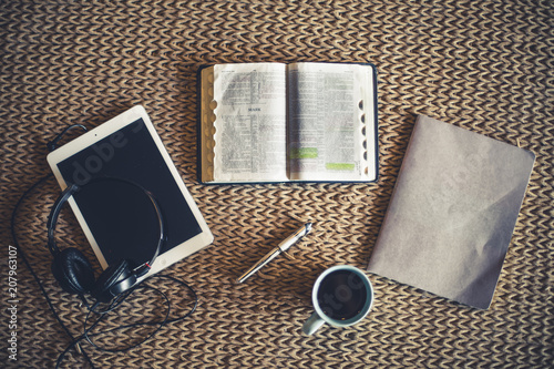 Shot from above of open Bible, coffee, notepad and tablet in front of fire place