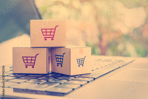 Online shopping / ecommerce and delivery service concept : Paper cartons with a shopping cart or trolley logo on a laptop keyboard, depicts customers order things from retailer sites via the internet. photo