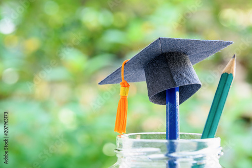 Education is the most powerful weapon or knowledge is power concept : Black graduation cap or hat with orange tassel on a pencil in a clear glass bottle, a green pencil with sharp tip points upward. photo