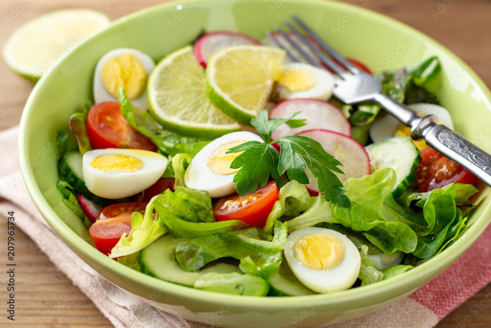 Fresh salad with vegetables and quail eggs on rustic wooden background