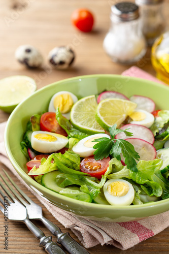 Fresh salad with vegetables and quail eggs on rustic wooden background