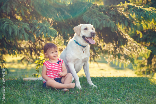 Portrait of cute adorable little Caucasian European baby girl sitting with dog in park outside. Child playing sitting by animal domestic pet. Happy childhood concept © anoushkatoronto