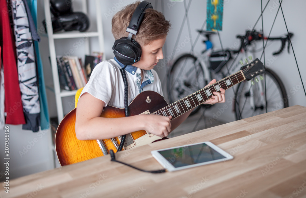 Kid boy learning to play electric guitar using tablet with headphones Stock Adobe Stock