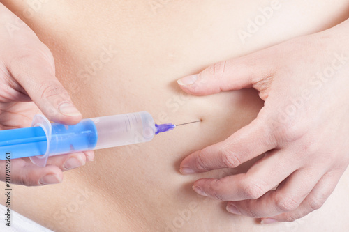 Woman is injecting hormones to belly with syringe. IVF concept.