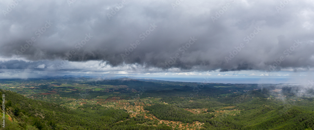 Mallorca, XXL panorama dark rainy clouds in the sky over green mountainous landscape on coastline of the island