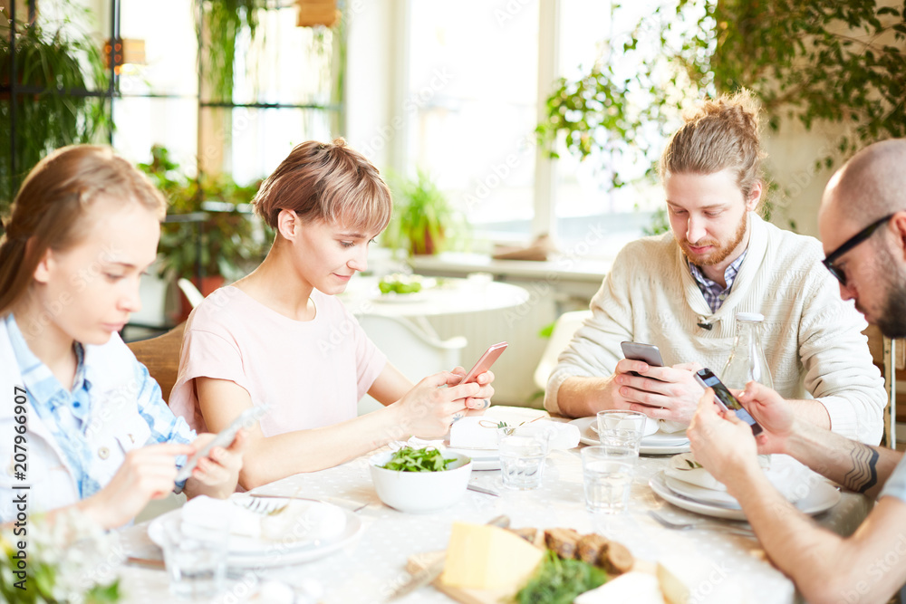 Friends gathering and using smartphone while waiting for order at restaurant