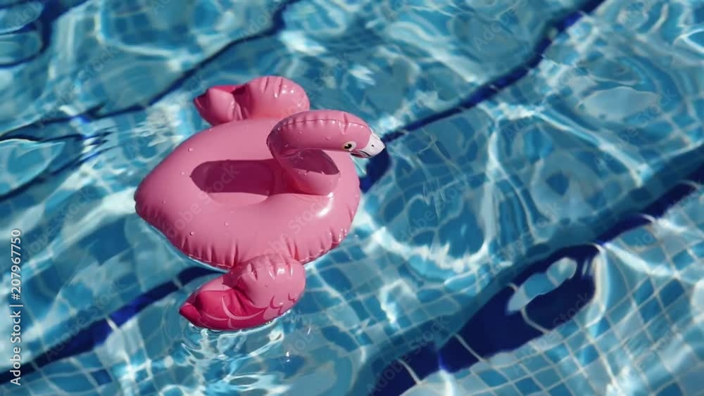 Empty inflatable flamingo floaties floating on pool water. Fun colorful floats waiting for a party on a hot summer day.