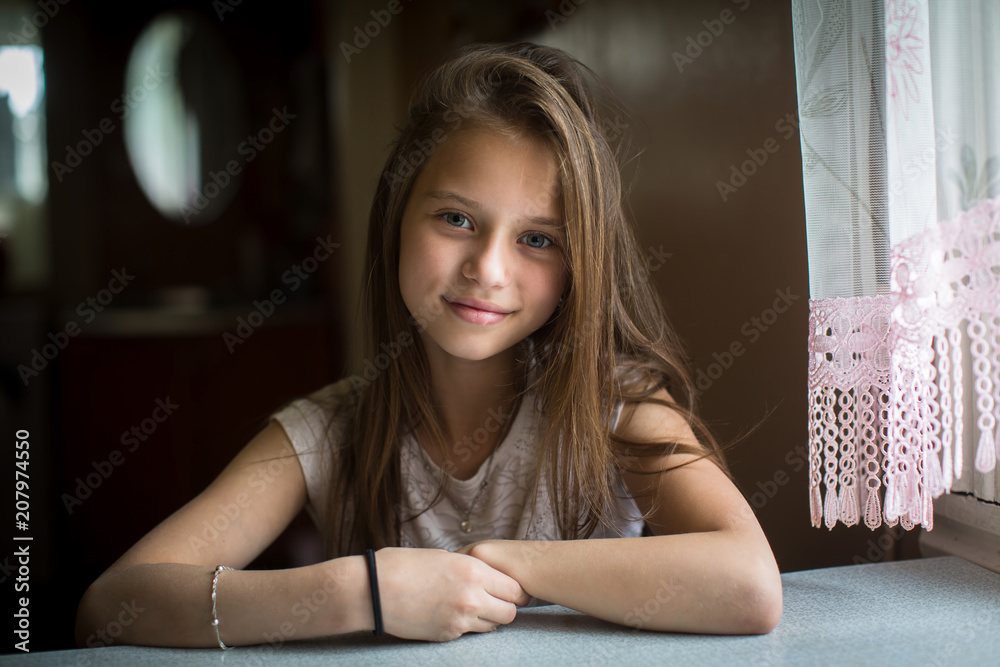 Portrait of cute ten-year-old girl posing for the camera sitting at the  table. Stock Photo