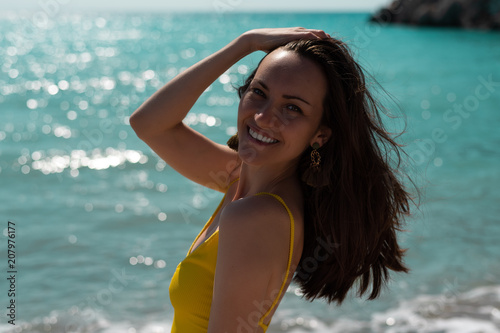 Large portrait in the hard light of the bright sun of a young woman on the sea in a yellow swimsuit, real life