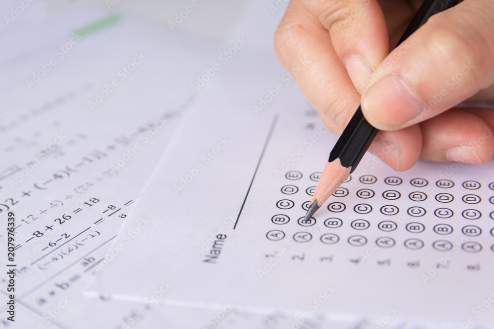 Students hand holding pencil writing selected choice on answer sheets and Mathematics question sheets. students testing doing examination. school exam Students hand holding pencil writing selected choice on answer sheets and Mathematics question sheets. students testing doing examination. school exam